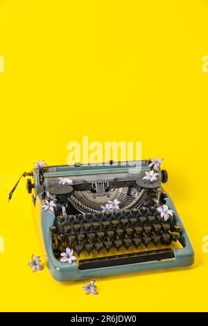 Vintage-Schreibmaschine mit Fliederblumen auf gelbem Hintergrund Stockfoto