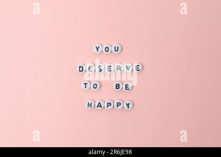 Draufsicht der Zitate „You deserve to be happy“ mit Perlen auf pinkfarbenem Hintergrund. Motivation und Erfolgskonzept Draufsicht von „Du verdienst es, glücklich zu sein“ Stockfoto