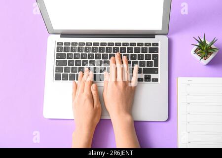Programmiererin mit Laptop mit Hauspflanze und Notebook auf violettem Hintergrund Stockfoto