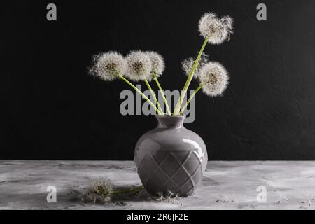 Vase mit wunderschönen Löwenzahnblumen auf dem Tisch vor dunklem Hintergrund Stockfoto