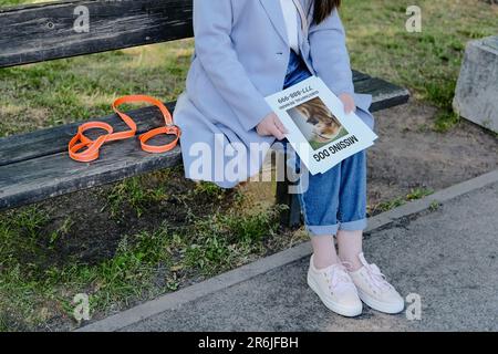 Der Hundebesitzer trauert, während er mit einem Halsband auf einer Bank sitzt und einen verlorenen Hundeflyer in der Hand hält. Haustier-Verwandte und Liebeskonzept. Stockfoto