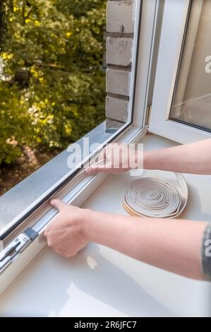 Ein Mann legt Dichtungsschaum auf das Fenster im Raum, um es warm zu halten. Das Konzept der Energieeffizienz. Stockfoto