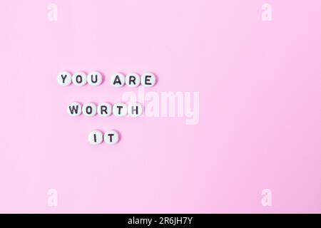 Draufsicht der Zitate „You're worth it“ aus Perlen auf pastellfarbenem Hintergrund. Motivation und Erfolgskonzept Stockfoto