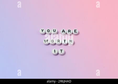 Draufsicht der Zitate „You're worth it“ aus Perlen auf pastellfarbenem Hintergrund. Motivation und Erfolgskonzept Stockfoto