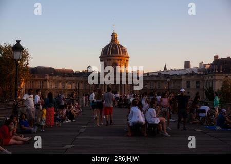 Paris, Frankreich - Juli, 14: Menschen, die am 14. Juli 2022 auf der Pont des Arts Artists Bridge von Paris mit dem Institut de France im Hintergrund spazieren gehen Stockfoto