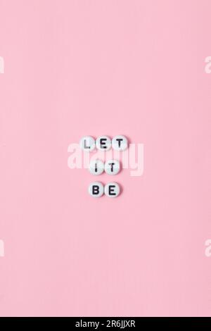 Draufsicht der Zitate „Let it be“ aus Perlen auf pinkfarbenem Hintergrund. Motivation und Erfolgskonzept Stockfoto