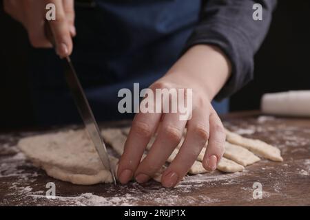 Eine Frau schneidet Teig am Holztisch, Nahaufnahme. Ich koche Grissini Stockfoto