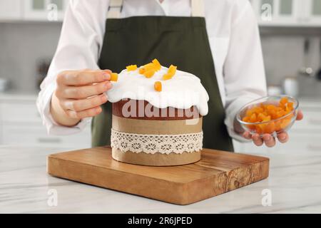 Frau dekoriert köstlichen Osterkuchen mit getrockneten Aprikosen auf einem weißen Marmortisch in der Küche, Nahaufnahme Stockfoto