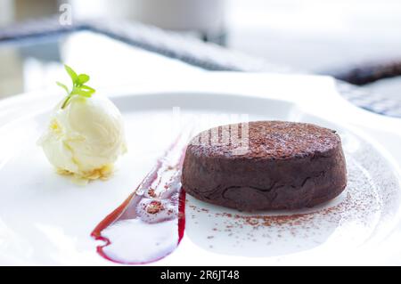 Vanille-Eiskugel mit Mandelscheibe und geschmolzenem Schokoladenkuchen auf weißem Teller Stockfoto