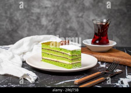 Kleine Scheibe bunter grüner Pistazienkuchen. Köstlicher Cremebrot auf dunklem Hintergrund Stockfoto