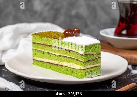 Kleine Scheibe bunter grüner Pistazienkuchen. Köstlicher Cremebrot auf dunklem Hintergrund. Schließen Stockfoto