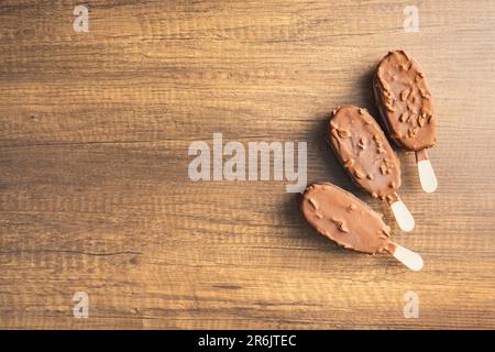 Eis am Stiel, mit Schokolade bedecktes Eis auf dem Holztisch. Draufsicht. Stockfoto