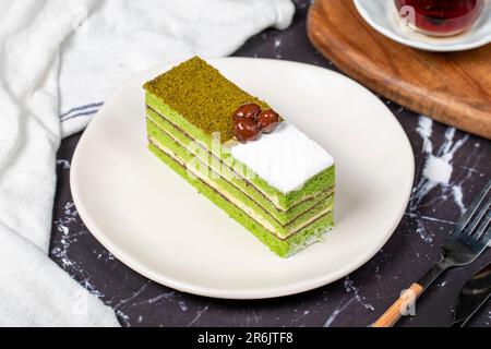 Kleine Scheibe bunter grüner Pistazienkuchen. Köstlicher Cremebrot auf dunklem Hintergrund Stockfoto