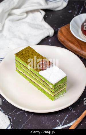 Kleine Scheibe bunter grüner Pistazienkuchen. Köstlicher Cremebrot auf dunklem Hintergrund Stockfoto