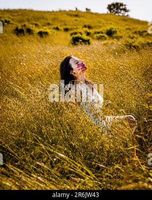 Junge Frau mit rotem Handabdruck im Gesicht, die auf einem Grasfeld sitzt Stockfoto