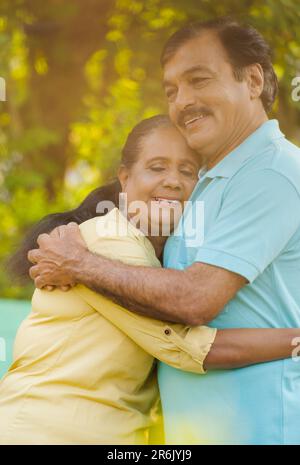 Vertikale Aufnahme einer Happy indian Seniorin, die den Ehemann umarmt oder umarmt, mit zusätzlichem Sonnenerscheinungseffekt - Konzept eines Begleiters Stockfoto