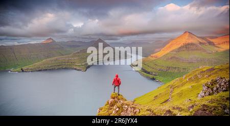 Ein Mann, der den Himmel im Morgengrauen betrachtet und auf Felsen über einem Fjord steht, Eysturoy Island, Färöer Inseln, Dänemark, Europa Stockfoto