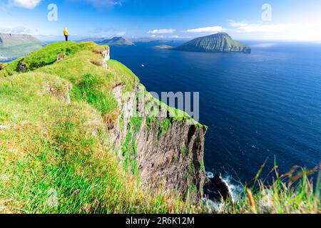 Eine Person bewundert die Aussicht, die auf Klippen über dem Ozean steht, Nordradalur, Streymoy Island, Färöer Inseln, Dänemark, Europa Stockfoto