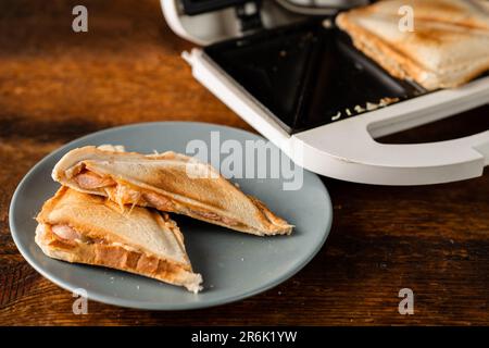 Frisch getoastete Sandwiches von einem Sandwichmaker auf einem Teller mit rustikalem Holzhintergrund. Getoastete dreieckige Sandwiches mit Käse.