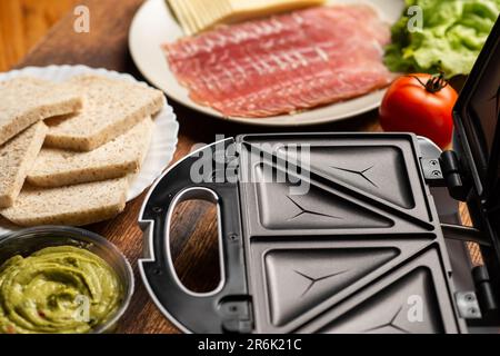 Sandwichmaker und verschiedene Zutaten auf Holzhintergrund. Ich koche Sandwiches. Stockfoto