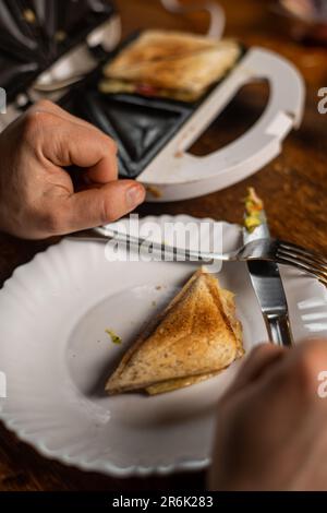 Ein unbekannter Mann isst Toast mit Guacamole. Frühstückszeit. Die Hände des Mannes halten einen Toast. Stockfoto