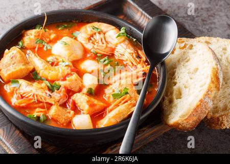 Meeresfrüchte und Fischeintopf wie Garnelen, Muscheln, Jakobsmuscheln, Tintenfisch mit Tomaten aus nächster Nähe in einer Schüssel auf dem Tisch. Horizontal Stockfoto