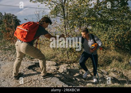Junger männlicher Wanderer hilft seinem Freund, auf die Straße zu kommen Stockfoto