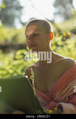 Umsichtige Frau mit Notebook in der Natur. Sonniger Tag, Sommerzeit. Remote arbeiten, freiberuflich arbeiten, online einkaufen. Stockfoto