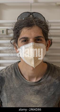 Eine junge Frau, die eine medizinische Gesichtsmaske trägt, steht vor einer Wand Stockfoto