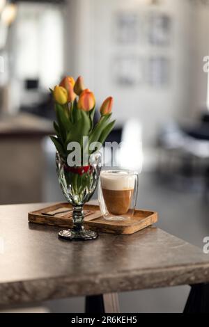 Ein Strauß orangefarbener Tulpen und eine Tasse heißer Kaffee liegen auf dem Tisch Stockfoto