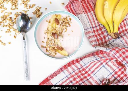 Eine Schüssel mit verschiedenen frischen Früchten, einschließlich zwei Bananen und Müsli, auf weißem Hintergrund Stockfoto