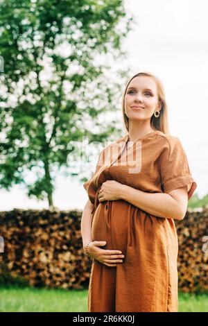 Außenporträt einer stilvollen schwangeren Frau in braunem Kleid Stockfoto