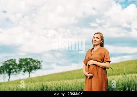 Außenporträt einer stilvollen schwangeren Frau in braunem Kleid Stockfoto