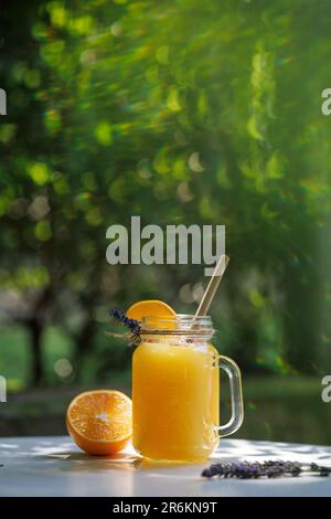 Orangenlimonade in einem Becher auf dem Tisch vor dem Hintergrund von natürlichem Grün Stockfoto