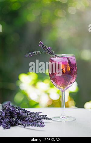 Ein Glas rosafarbener Cocktail mit Eis und Lavendel auf dem Tisch vor dem Hintergrund von natürlichem Grün Stockfoto