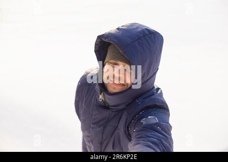 Ein Mann in Winterkleidung gibt seine Hand, um zum verschneiten See zu gelangen. Europäisches weißes, lächelndes männliches Lifestyle-Porträt, positive Emotionen. H Stockfoto