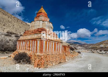 Farbenfroh gemalte buddhistische Stupa vor der Berglandschaft, erodierte Landschaft und Häuser von Garphu dahinter Stockfoto