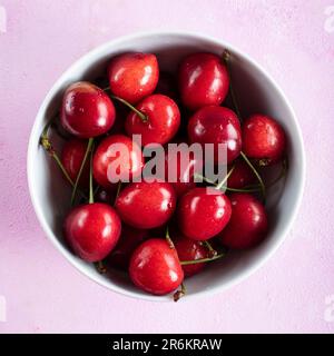 Frische Kirschfrüchte in weißer Schüssel auf pinkfarbenem Hintergrund. Stockfoto