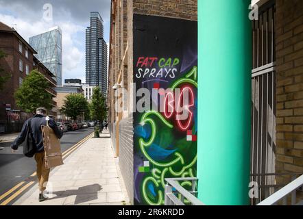 London, Großbritannien - Mai 17 2023: Ein Künstler mit seinem Portfolio geht in Shoreditch die Straße entlang. Die hohen Gebäude des Finanzviertels liegen vor uns. Stockfoto