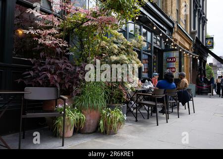 London, Großbritannien - Mai 17 2023: Gäste sitzen und entspannen an einem Café-Tisch im Freien im Flat Iron Restaurant in Spitalfields, East London. Stockfoto