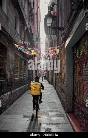 Barcelona - 10. Juni 2023: Glovo Liefermann auf einem Fahrrad, der durch die engen Gassen von Barcelona verteilt wird Stockfoto