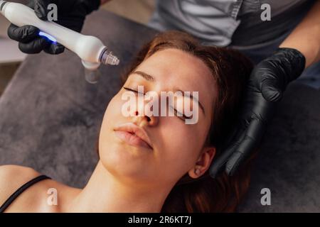 Kaukasische Frau bekommen Gesichtspeeling Verfahren in einer Schönheitsklinik, Nahaufnahme. Verjüngende Gesichtsgasbehandlung. Hydro Air Haut Reinigung Operat Stockfoto