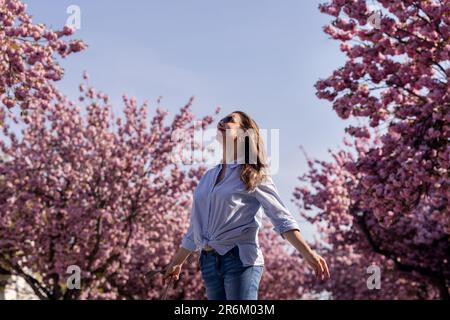 Schöne lächelnde Frau vor dem Hintergrund von lila rosa Kirschblüten Stockfoto