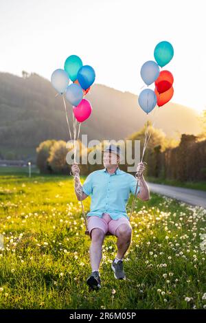 Ein Mann schwingt auf einer Schaukel in Ballons Stockfoto
