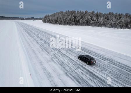 Ein Auto, das auf einer Eisstrecke auf einem gefrorenen See in der schneebedeckten Landschaft fährt, Jokkmokk, Norrbotten, Lappland, Schweden, Scaninavia, Europa Stockfoto