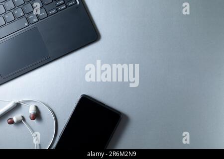 Die Ecke von Tastatur, Smartphone und Kopfhörern liegt auf einem beleuchteten Tisch mit einem Platz zum Kopieren Stockfoto