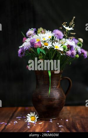 Dunkelbraune Vase mit Wildblumen auf einem Holztisch auf dunklem Hintergrund Stockfoto