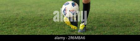 Banner 1x4 mit den Füßen eines jungen Fußballspielers in Schuhen und mit einem Ball auf dem Fußballfeld Stockfoto