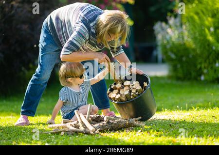 Seniorin und ihr Enkel sammeln trockene Brennholzstämme. Trocken gehackte Brennholzstämme, die übereinander in einem Stapel gestapelt sind. Stockfoto