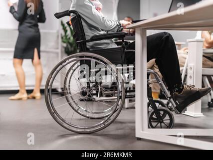 Person im Rollstuhl, die im Büro an ihrem Laptop arbeitet Stockfoto